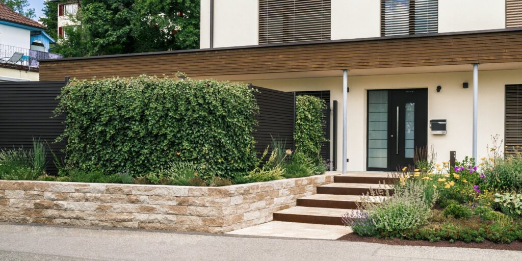 Moderne Gartengestaltung in Tuttlingen-Möhringen mit gepflegten Formgehölzen, Natursteinmauer und harmonisch gestaltetem Hauseingang.